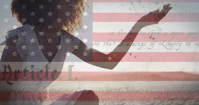 Constitution text over american flag against african american woman playing with sand at the beach