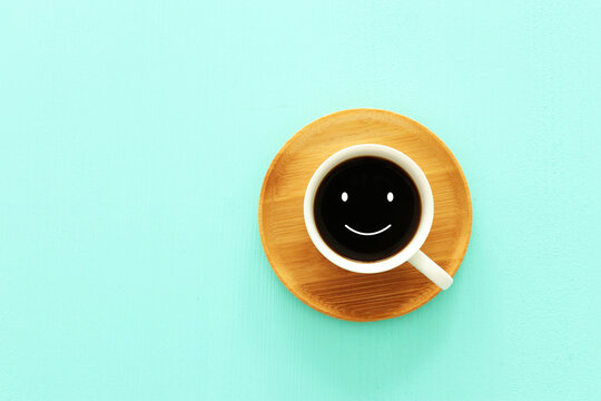 Top view image of coffe cup with happy face on wooden mint background. Flat lay.