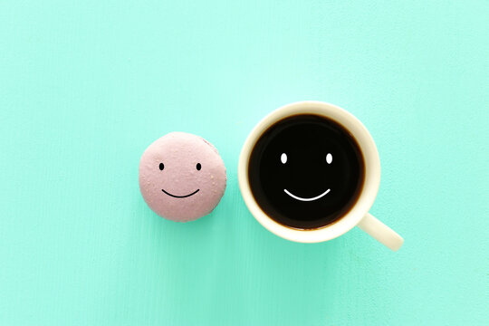 cup of coffee and colorful macaroon with happy face on wooden mint background
