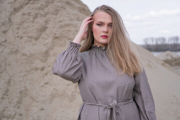 Beauty portrait of a young blond girl in a vintage dress. She is posing on a sandy landscape.