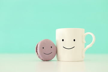 cup of coffee and colorful macaroon with happy face on wooden mint background
