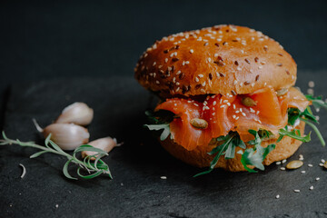 Appetizing burger with smoked salmon and arugula served on black stone board