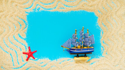 Sand frame with a miniature ship and red starfish on a blue background. Flat lay. Top view. Copy space. Vacation concept. Travel concept.