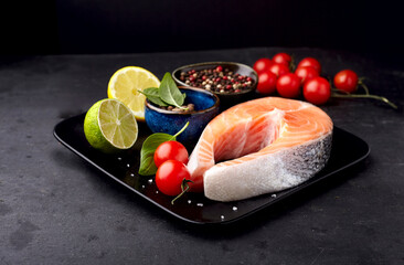 Salmon fish in the black plate with fresh  basil, citrus, tomatoes  and spices.  Steak on black background.