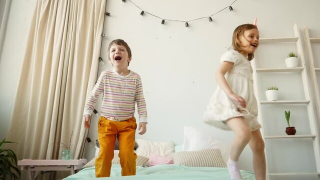 Young kids having a fun time jumping on the bed, brother and sister jump, play together, happy children, family concept.