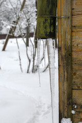 large icicles on the roof of a wooden rural house, village