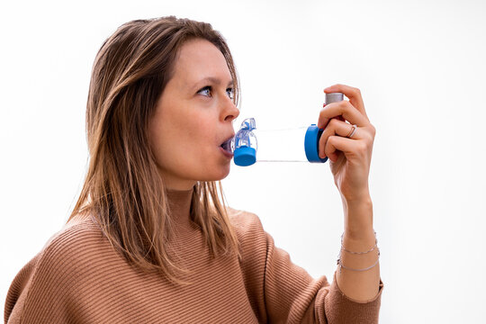 Young Women Taking Asthma Medication With An Inhaler And Spacer