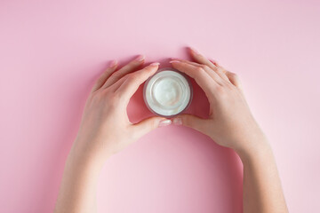 Nourishing cream and beautiful female hands on pink background. Skin care concept. Image for advertising and design.