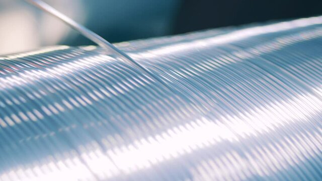 Close up view of silver wire unwinding from a big spool