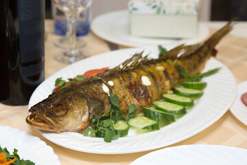 Large fried fish on a platter with vegetables and herbs.