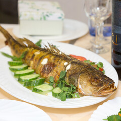 Large fried fish on platter with vegetables and herbs.