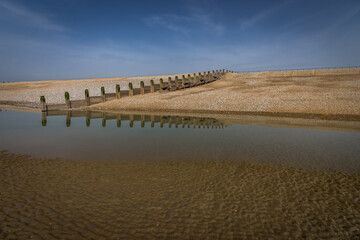 Fototapeta na wymiar Reflections of groynes on the beach at Camber, East Sussex, England