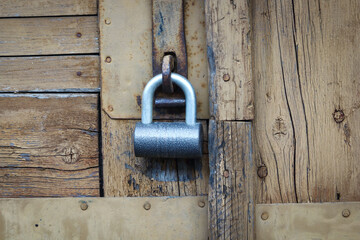 Metal padlock hanging on locked wooden door