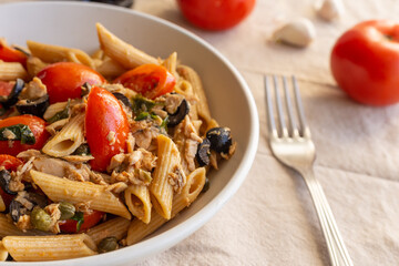 Penne pasta with tuna, capers, tomato and black olives. Typical italian dish.