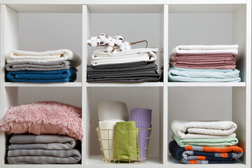 Stacks of towels, sheets, bed linen, blankets and pillows on a white shelf.