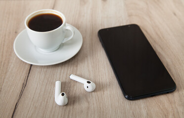 Fototapeta na wymiar Smartphone, wireless earphones, coffee on wooden background.