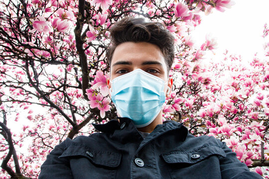 Selfie of young man wearing protective face mask with cherry blossom in the background 