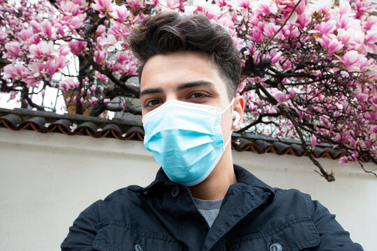 Selfie of young man wearing protective face mask with cherry blossom in the background 