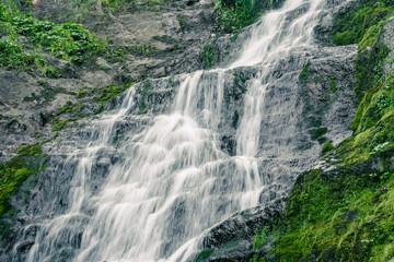 Atmospheric view of waterfall on river in rainforest. Swift stream among rocks and green moss.