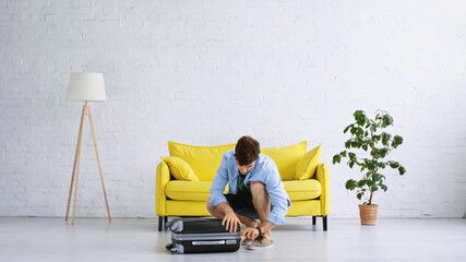 man in blue shirt zipping luggage in living room