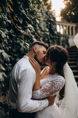 Fototapeta premium Walk of the newlyweds near the stone mansion. Warm summer evening. Portrait of the bride and groom. Evening photo session.