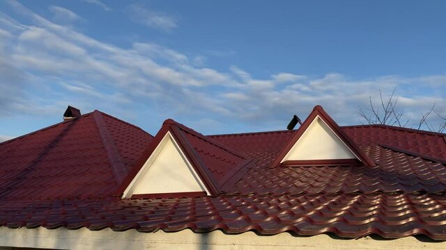 Static image of red metal roof of house in sunny day on background of blue sky.
