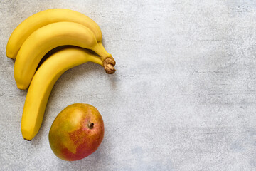 Bunch of bananas and mangoes on a gray background with copy space