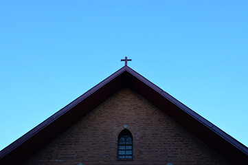 Church Roof with a cross. Church building roof with holy cross. Cloudy moody blue sky background. Minimal architecture design and detail. Exterior design and detail. 