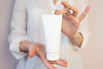 Fototapeta na wymiar woman in a white shirt holds a white tube of cream in her hands