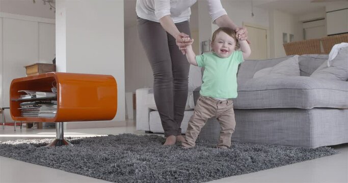 baby boy happy about taking his first steps with help of mum slow motion