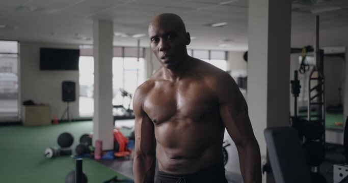 Muscular black man in gym flexes pecs after workout and looks up at camera