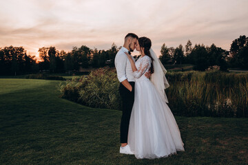 Walk of the newlyweds in the park. Warm summer evening. Portrait of the bride and groom. Evening photo session.