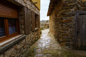Narrow alley between stone houses with light in the background and reflections on the ground wet from the rain.