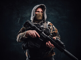 Serious army soldier wearing hood and camouflage clothes holding rifle