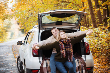 young couple sitting in the trunk of a car on the road in autumn