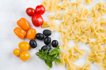 Pasta ingredients, raw pasta, cherry tomatoes, olives and basil leaves