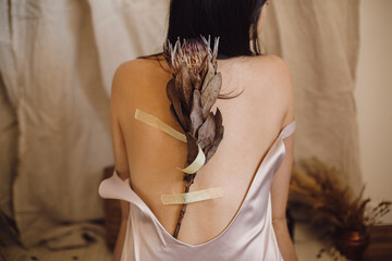 Dry protea flower duct-taped on female skin on back. Sensual woman with protea. Self care concept