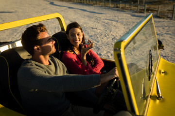 Caucasian couple sitting in beach buggy by the sea during sunset talking by phone