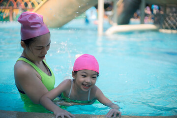 Asian mother and daughter in swimming pool, aquapark. Sunny summer.