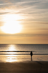 A silhouette of a woman walking on a black beach during sunset. The photo is taken in Akranes in Iceland 
 where swimming in the sea is popular all year around.