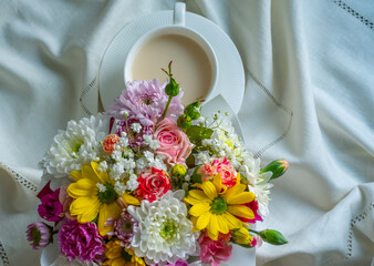 Bouquet of colorful flowers with a white cup on a white tablecloth