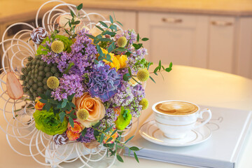 Romantic background with a cup of tea, lilac flowers and a book over a white wooden table. Leisure concept, spring breakfast, a bouquet of spring flowers, a cup of cappuccino and a book on the table,