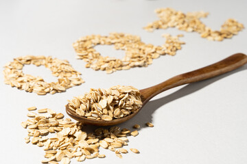 Word OAT made of flakes and oat on wooden spoon on grey background