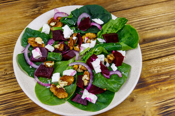 Tasty spinach salad with boiled beetroot, feta cheese, walnut and red onion on wooden table. Healthy vegetarian food
