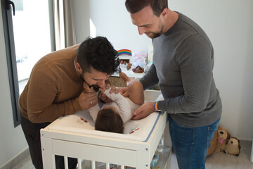 Gay married couple changing their daughter´s diaper in the bedroom.