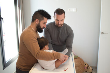 Fototapeta premium Gay married couple changing their daughter´s diaper in the bedroom.