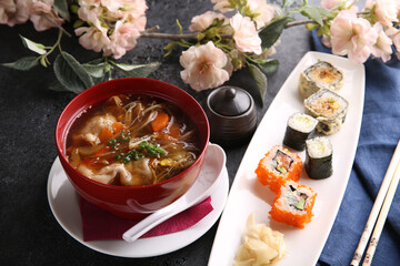 Japanese cuisine. Assorted rolls and sushi with ginger with soup in bowl on a white plate on a black table with soy sauce. Chopsticks, sakura. Restaurant menu. Background image, copy space