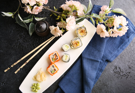 Japanese cuisine. Assorted rolls and sushi with ginger on a white plate on a black table with soy sauce. Chopsticks, sakura. Restaurant menu. Background image, copy space