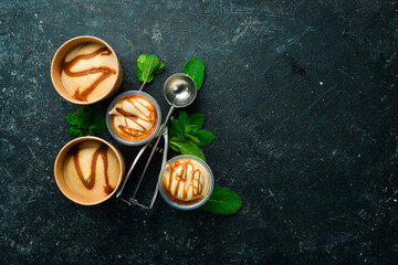 Caramel ice cream with mint and salted caramel. Ice cream spoon. On a black stone background, top...