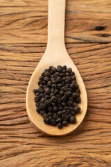 Closeup of black pepper grains on a wooden spoon. Food backdrop